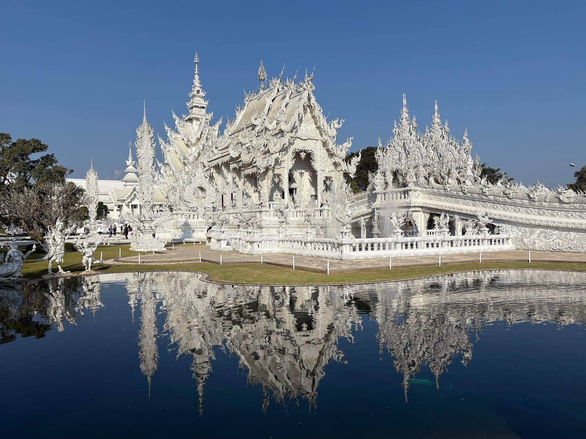 The all-white Wat Rong Khun temple reflected in a pond