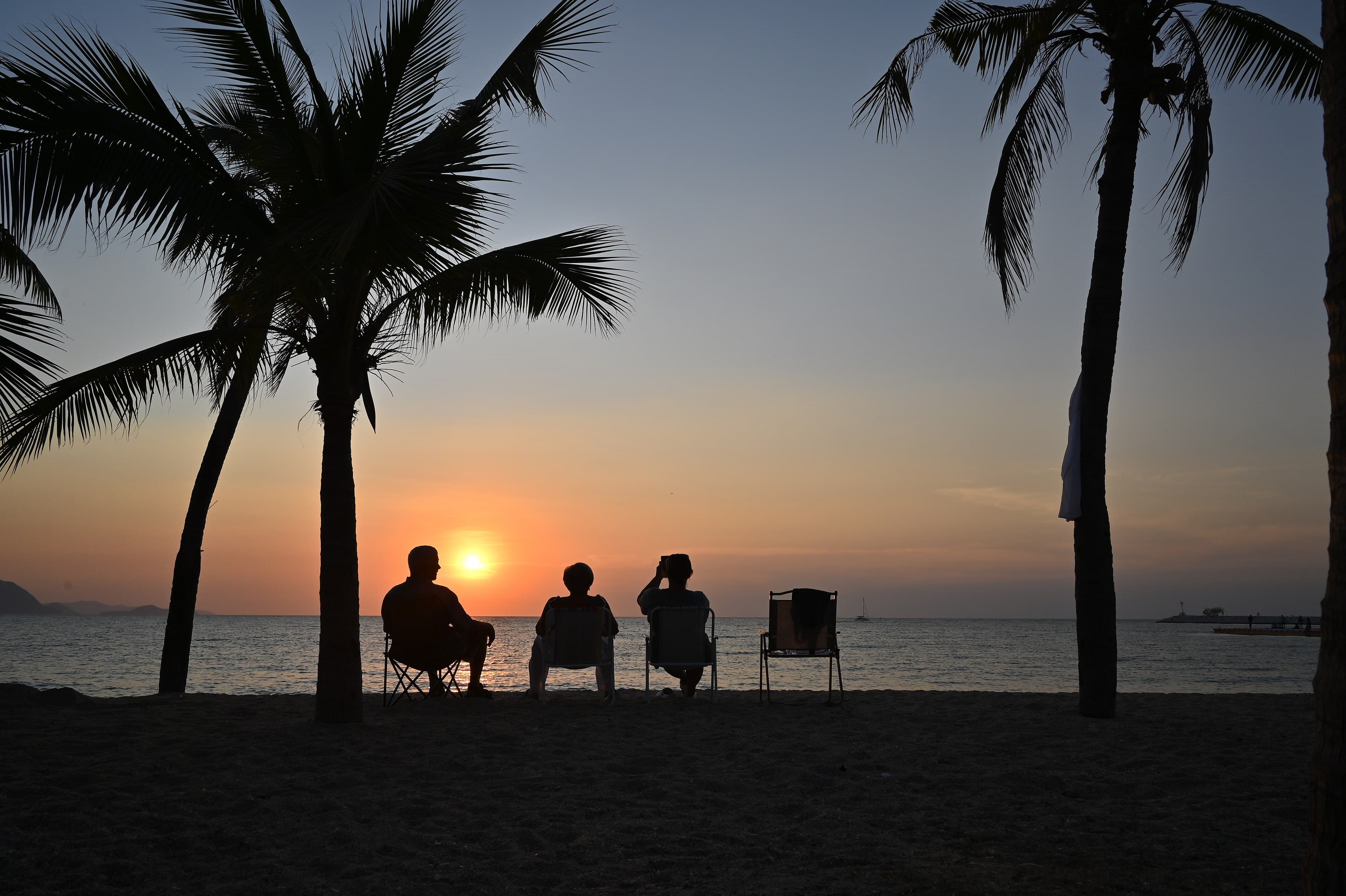 Three family members silhouetted against a tropical sunset, relaxing under palm trees